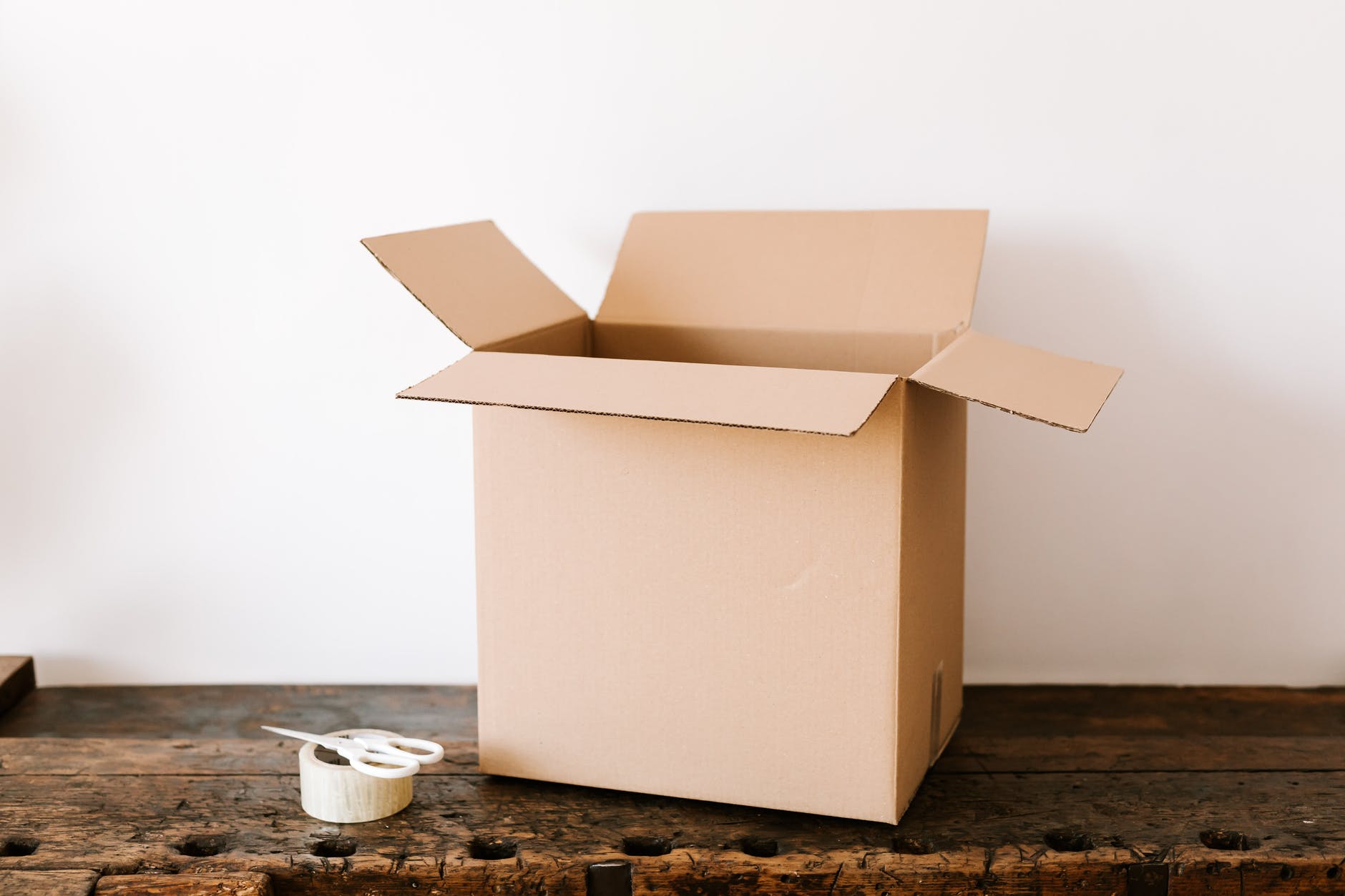 cardboard box on dark wooden table near tape and scissors