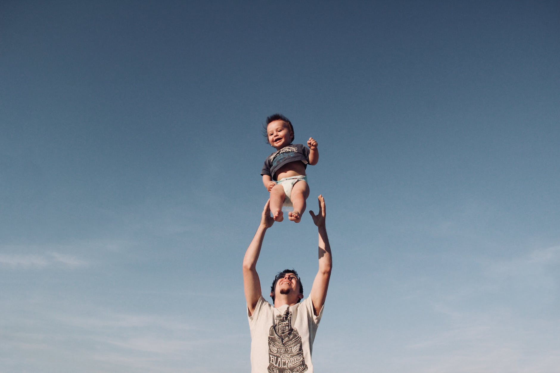 photo of a man raising baby under blue sky